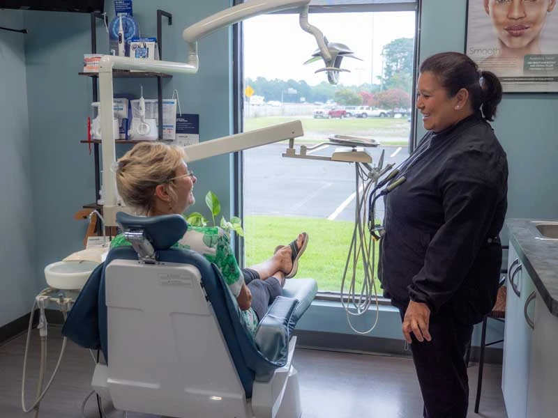 A patient sitting in an exam chair speaking with a friendly staff member about cosmetic dentistry options at Virgina Beach, VA